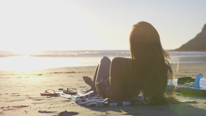Lady relaxes on the beach at sunset next to the ocean