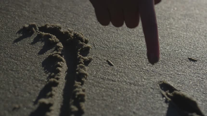 Person draws a heart in wet sand with their finger