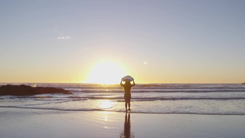 A woman carrying a surfboard on her head is walking towards the ocean