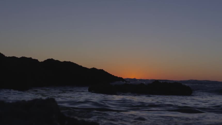 Ocean waves crash into a rocky shore at dusk