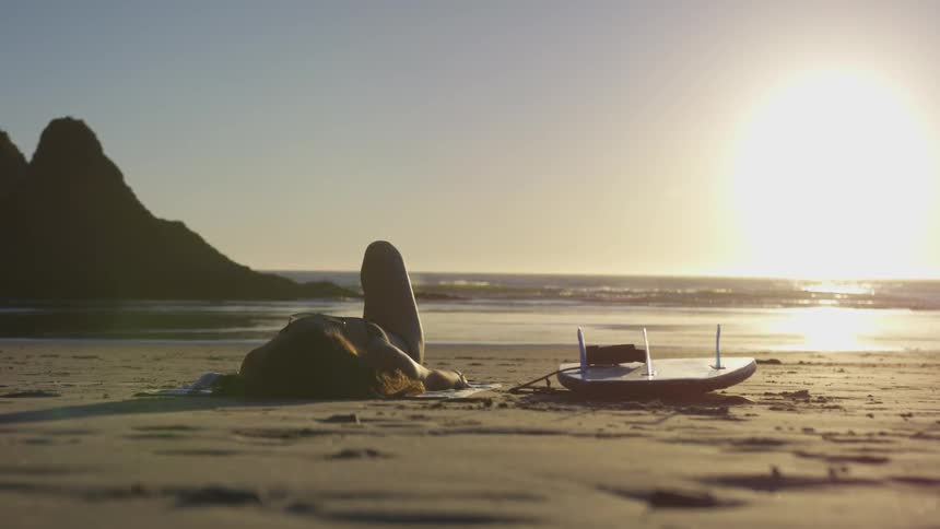 Woman lying on the beach with a surfboard by her side