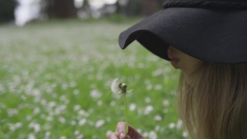 Woman with blonde hair blows on a dandelion in a field