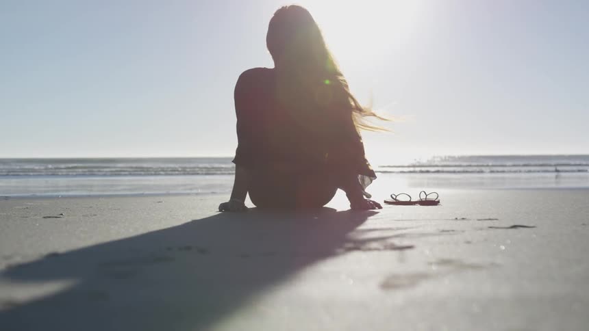 A woman sitting on a beach with her hair blowing in the wind
