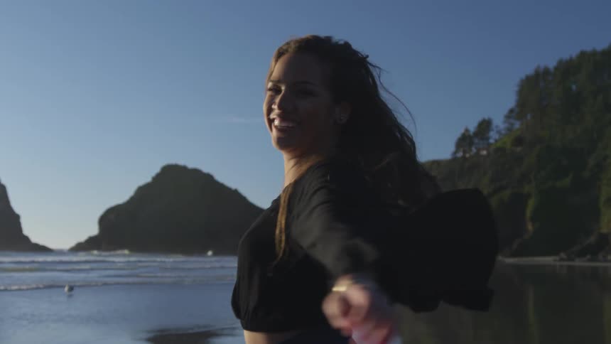 A woman jumping up and down at turning around on the beach at sunset next to the ocean