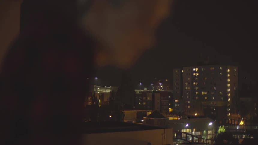 Man stands on a balcony overlooking the city at night