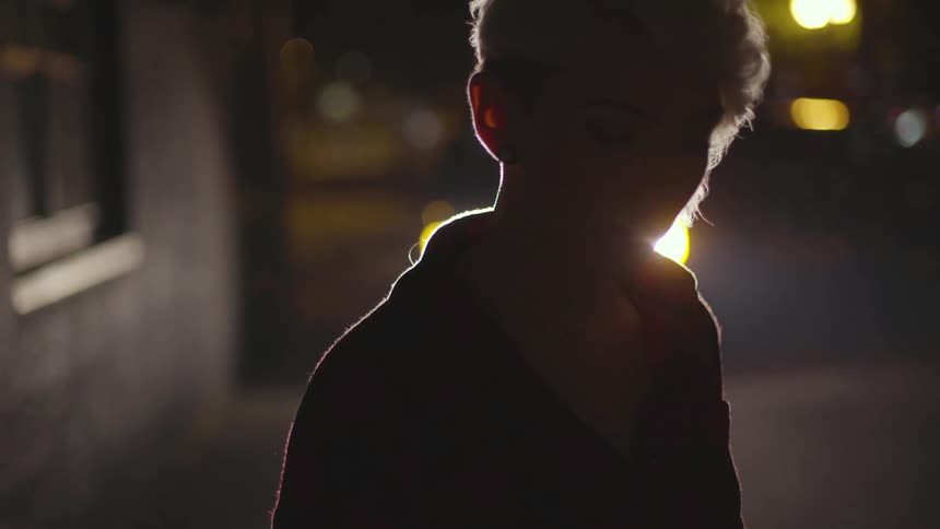 A car's headlights shine on a woman standing alone