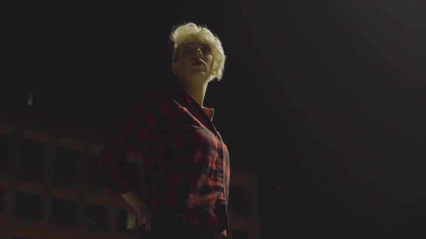 Blonde woman with short hair standing on the street at night