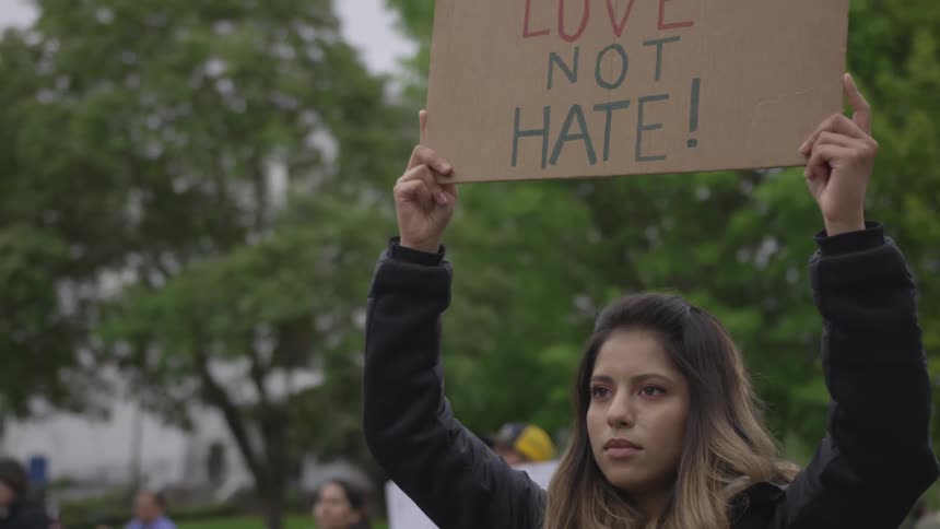 A hispanic female protester holding up a cardboard sign