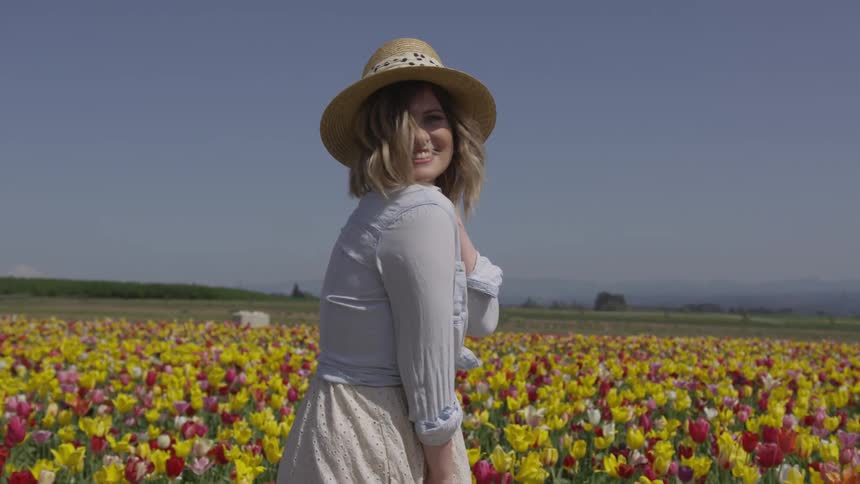 A woman walking through a field of flowers turns and smiles