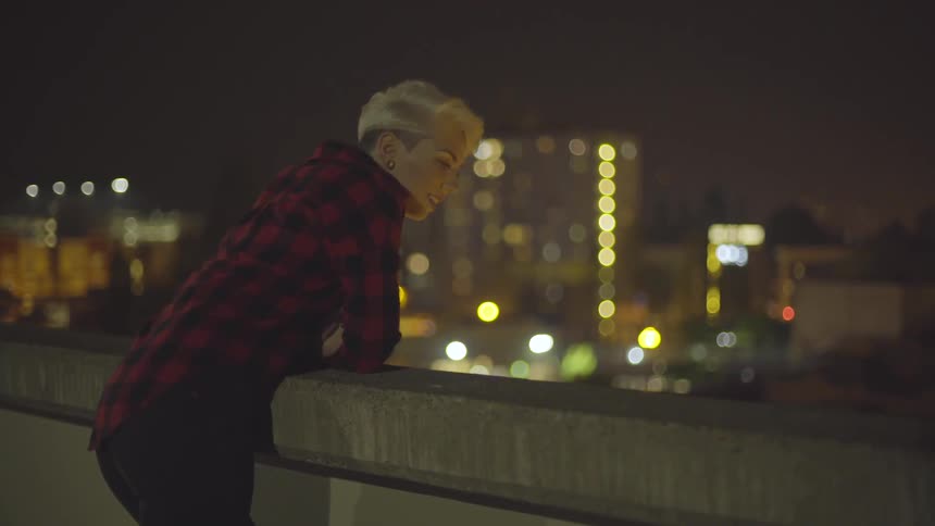 A woman leaning on a concrete railing of a balcony at night