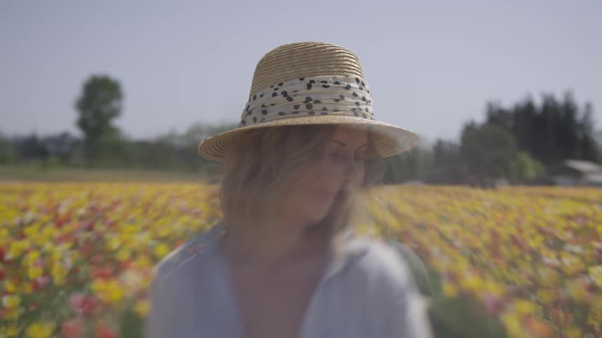 She's sitting in a field of tulips wearing a hat first she looks sad then she is kinda happy