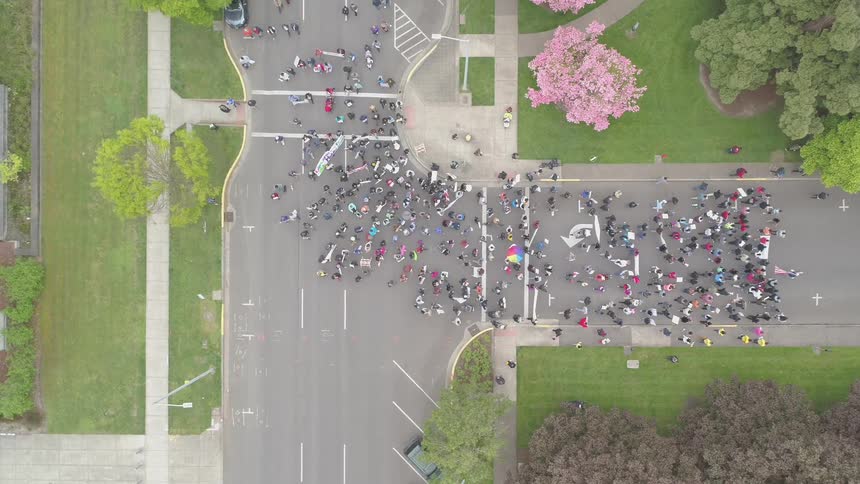 A parade of people march down a street turning left at an intersection