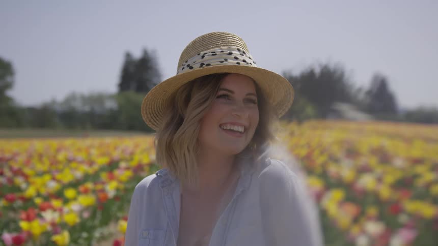 A woman in a sun hat standing a field of flowers during the day