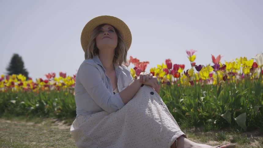 A woman looking to the sky beside a field of flowers