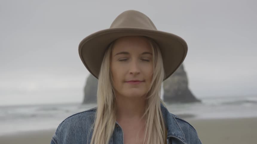 A woman wearing a hat standing by the beach