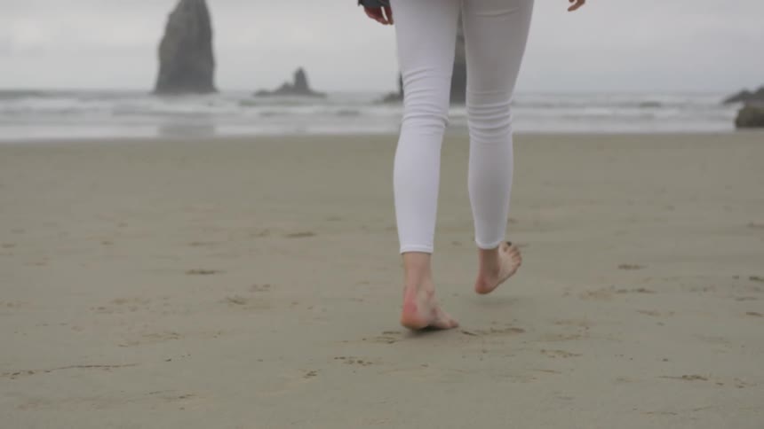 Woman wearing white pants walks bare feet on the sand at beach next to the sea