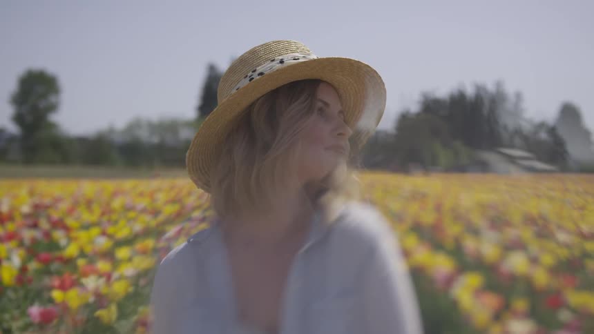 A woman in a sun hat looks around while standing in a field of flowers