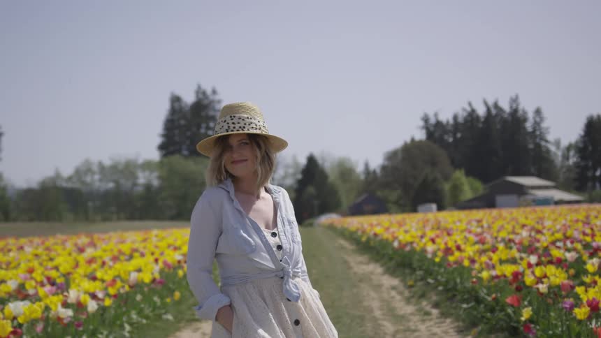 Woman in white dress and hat spins and smiles for camera in tulip field