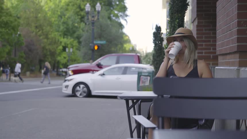 A young blonde woman sits at a table drinking a coffee