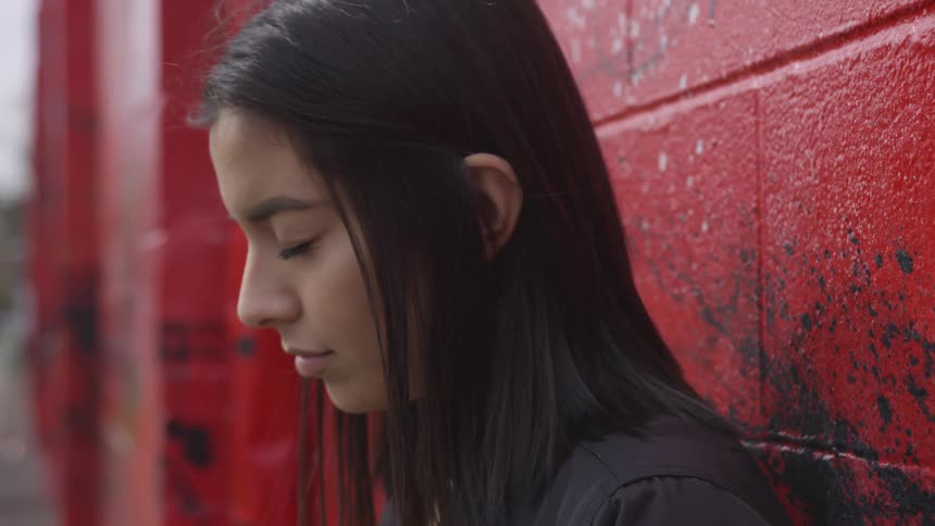 White woman closing her eyes while leaning against red wall