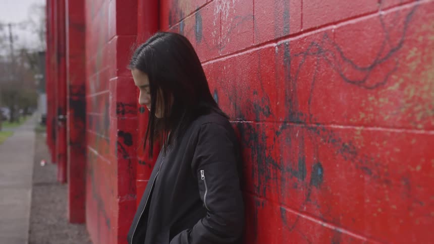 A young woman in black leaning against a red painted stone wall