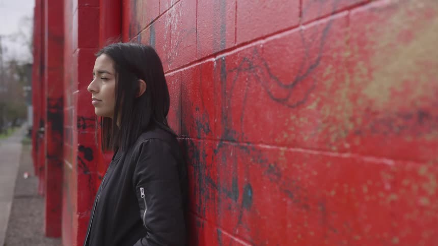 A woman stands against the wall of a building