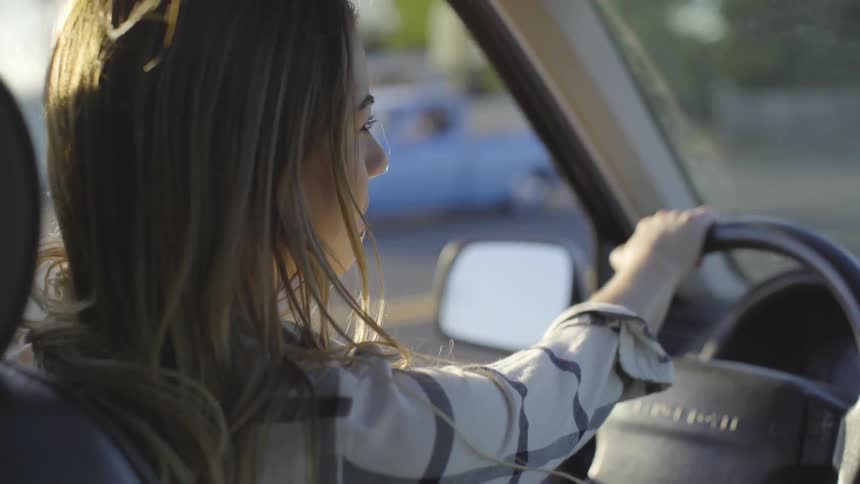 A young woman sits in her car driving