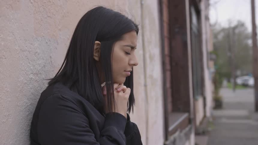 A young woman leans against a wall with her eyes close
