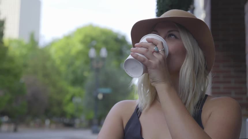 A woman sits smiling and drinking a coffee