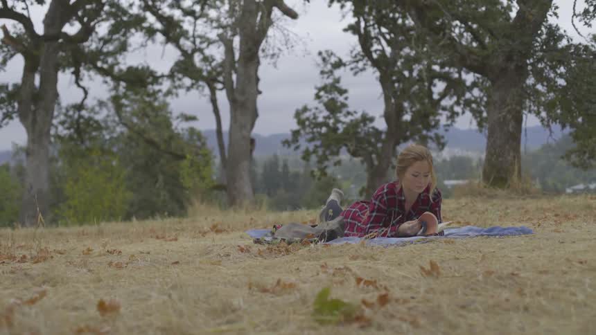 Woman lays on blanket in field and reads