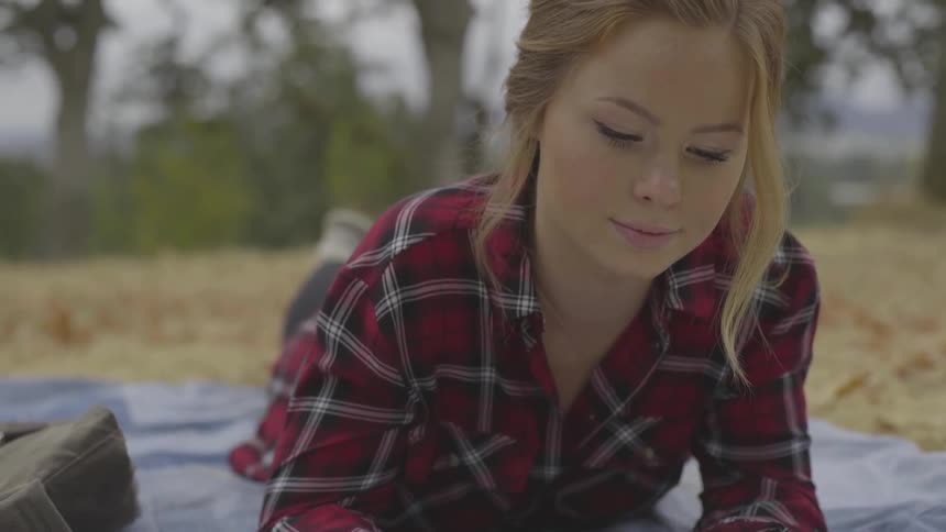 Blonde woman who wears striped shirt lies on her stomach in the forest by day