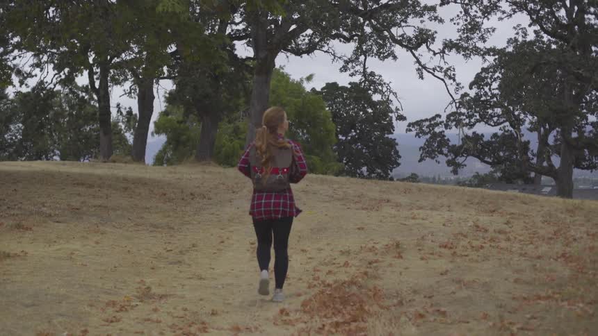 A woman hikes through a grove wearing a backpack and looks side to side