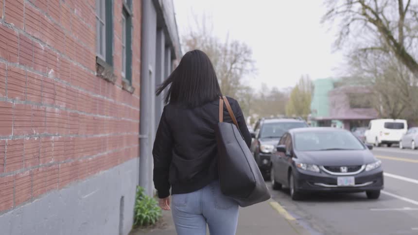 Woman walks down sidewalk between building and street