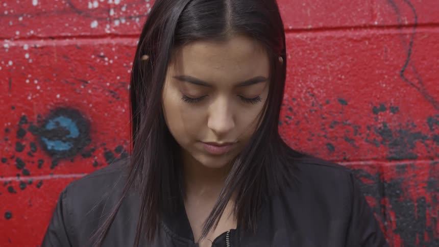 Woman stands and closes eyes in front of red wall in the daytime