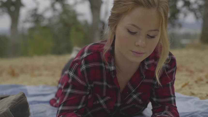 White woman reading a book while laying down in the middle of a grass field