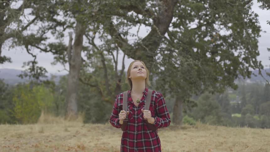 Woman with a backpack standing on a field near trees
