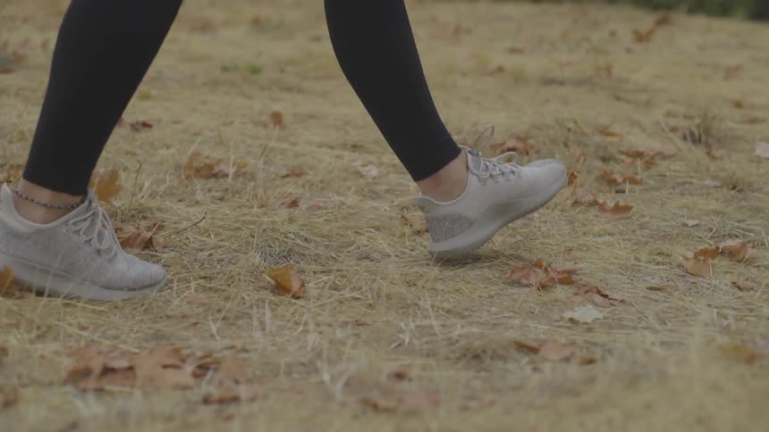 A woman walks through dead grass and leaves