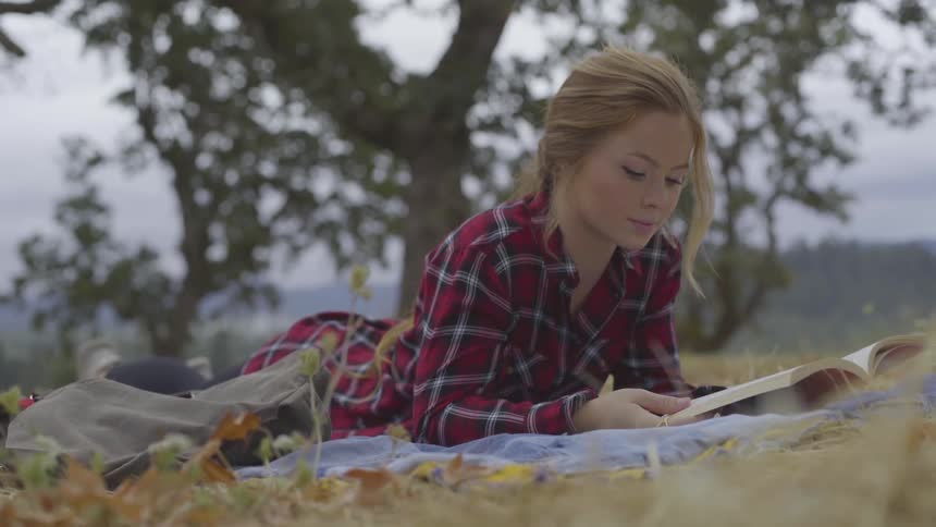 Young woman lying on a towel over a grass reading a book
