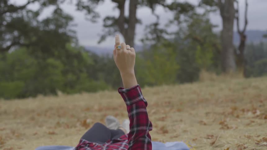 A woman lies on the ground and points her finger straight up into the air