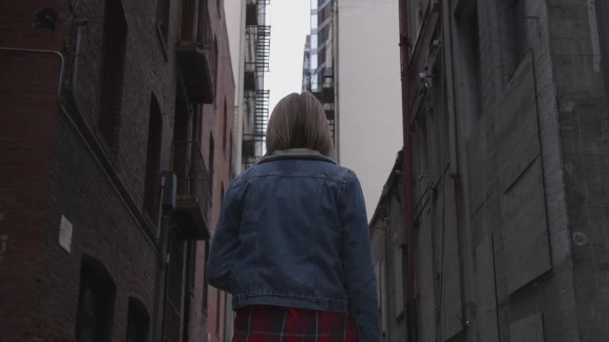 A woman stands in the street between buildings