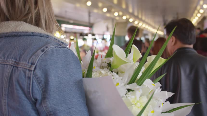 Blonde young woman holding a bunch of flowers walks behind a group of people in a store