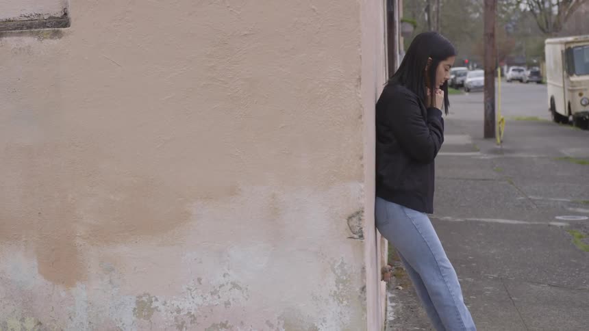 Woman praying while leaning against the wall at the street