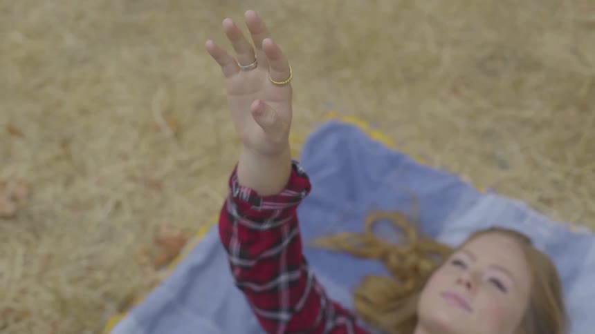 A woman is laying outdoors and pointing at the sky