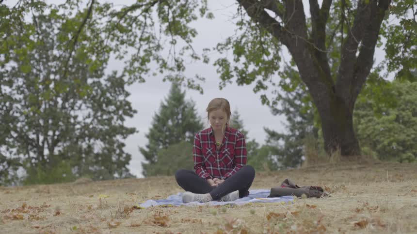 Woman who wears striped shirt sits in a cross legged position in the forest in the daytime