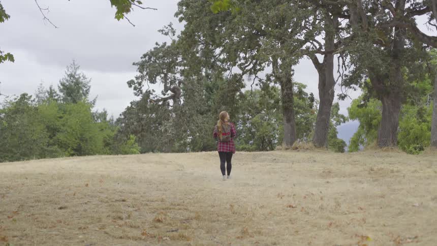 A woman walking on bare ground near a lot of trees