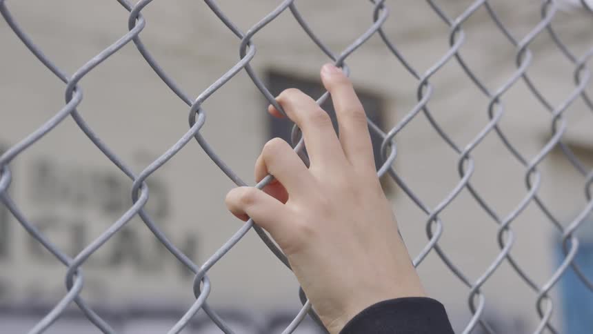 Caucasian hand grasps the chain link fence