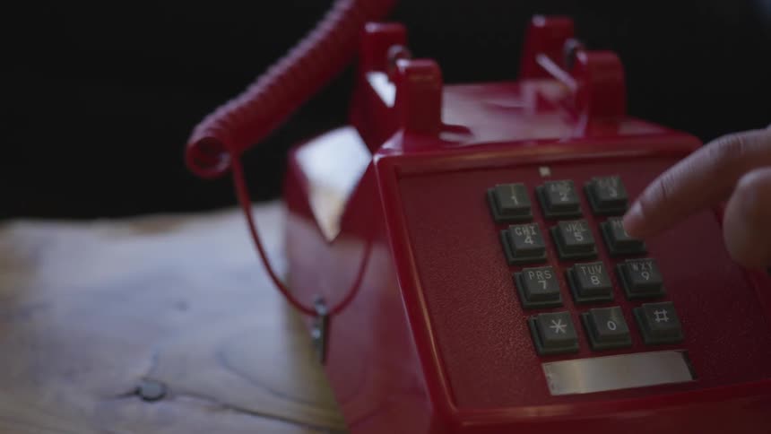 A person picks up the receiver of a phone and dials numbers