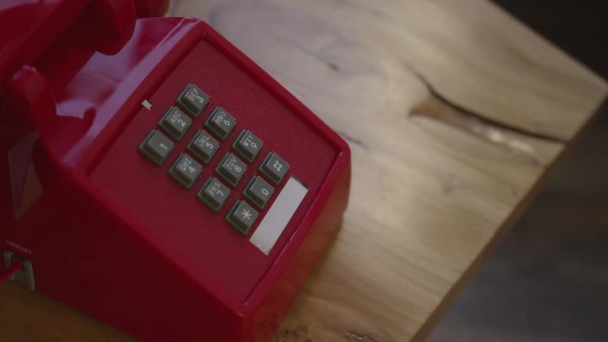 An old red touch tone phone sits on a wooden table