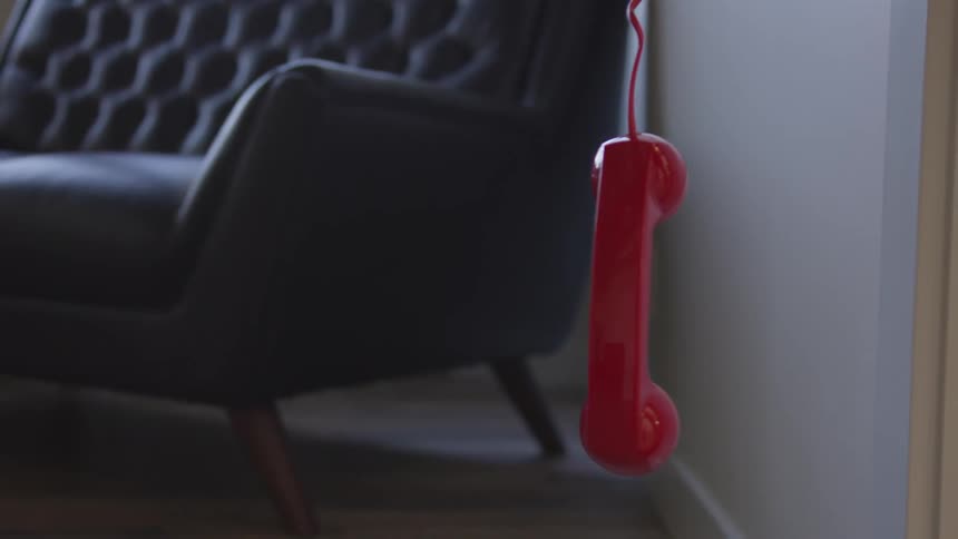 Red telephone receiver hangs from a cord near a chair