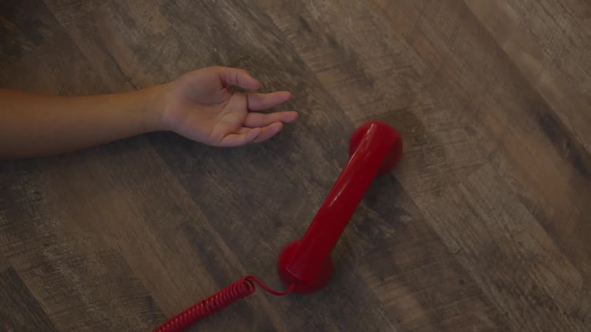 The handset of the red vintage phone skitters out of the young hand and skitters across the floor